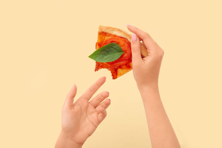 Woman holding slice of bitten pizza on yellow background