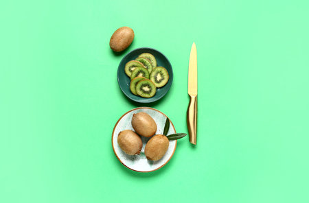 Plate and bowl with fresh kiwi on green backgroundの写真素材