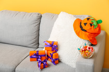 Sofa with gift boxes, tasty candies and hat for Halloween near orange wall in living room, closeupの写真素材