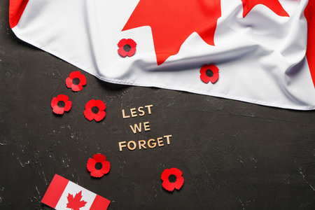 Poppy flowers with flags of Canada and text LEST WE FORGET on grunge black background. Remembrance...