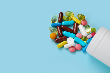 Jar with different scattered pills on blue background