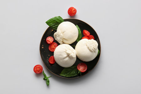 Plate of tasty Burrata cheese with basil and tomatoes on white backgroundの写真素材