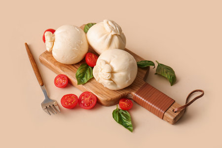 Wooden board of tasty Burrata cheese with basil and tomatoes on beige backgroundの写真素材