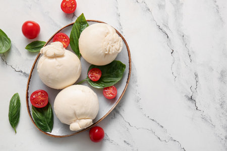 Plate of tasty Burrata cheese with basil and tomatoes on white backgroundの写真素材