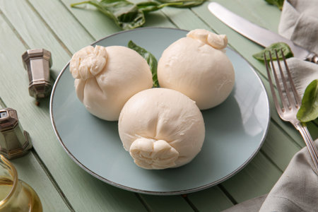 Plate of tasty Burrata cheese with basil on green wooden table