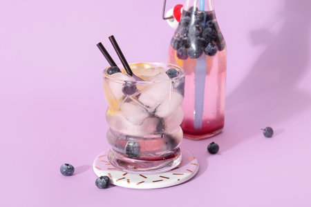 Glass and bottle of fresh blueberry lemonade on lilac backgroundの写真素材