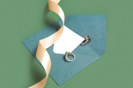 Envelope with greeting card, rings and golden ribbon on green backgroundの写真素材