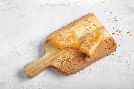 Wooden board with fresh honeycombs and bee pollen on light backgroundの写真素材