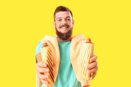 Portrait of happy young man with tasty hot dogs on yellow backgroundの写真素材