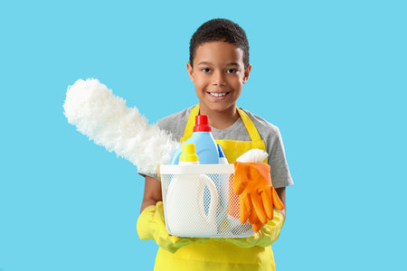 Little African-American boy with cleaning supplies in basket on blue backgroundの写真素材
