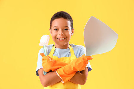 Little African-American boy with cleaning supplies on yellow backgroundの写真素材