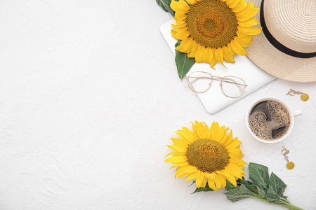 Beautiful sunflowers, cup of coffee, accessories and modern laptop on light backgroundの写真素材