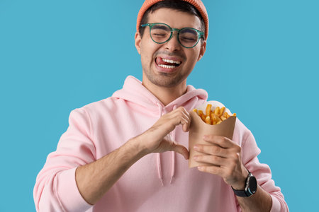 Young man with french fries making heart gesture on blue background, closeupの写真素材