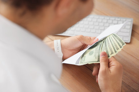 Young businessman with envelope of money in office, closeup