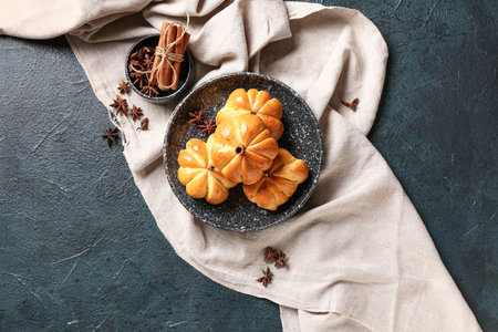Bowl with tasty pumpkin shaped buns on black background