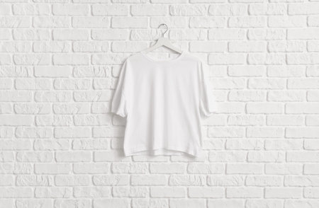 Stylish t-shirt hanging on white brick wall