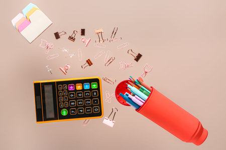 Pencil case with different stationery and calculator flying on color background