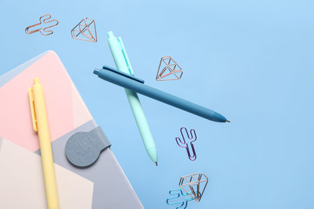 Notebook, pens and paper clips flying on color background