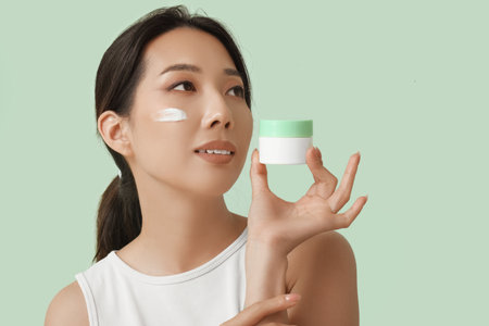 Beautiful young Asian woman with cream on her face against turquoise backgroundの写真素材