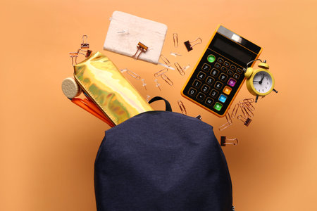 School backpack with stationery flying on color background