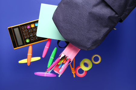 School backpack with different stationery flying on blue background