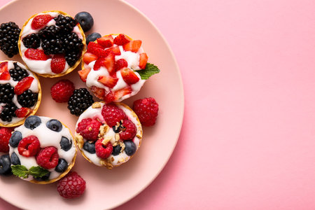 Plate of tasty tartlets with whipped cream and berries on pink backgroundの写真素材