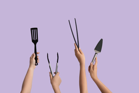 Female hands with tongs and spatulas on lilac backgroundの写真素材