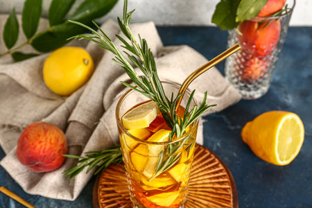Wooden board with glass of fresh peach lemonade and rosemary on blue tableの写真素材