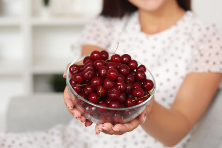 Beautiful young woman with bowl of ripe cherries in living roomの写真素材