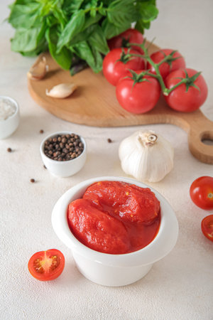 Bowl of canned tomatoes and spices on light background
