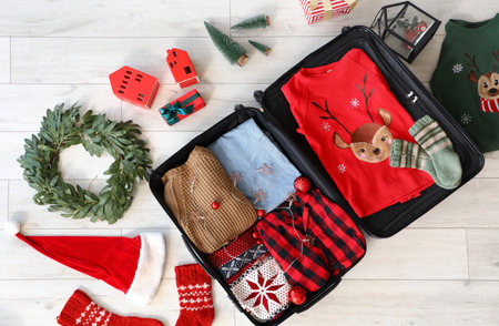 Open suitcase with Christmas clothes on light wooden floor, top viewの写真素材