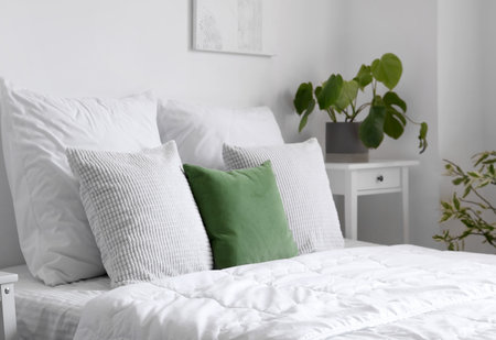 Cozy bed with white blanket and pillows in light bedroomの写真素材