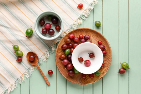 Plate and bowls with fresh gooseberries on green wooden backgroundの写真素材