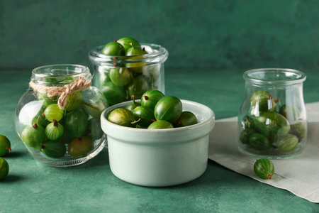Bowl and jars with fresh gooseberries on green backgroundの写真素材