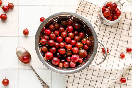 Colander and jar with fresh gooseberries on white tile backgroundの写真素材