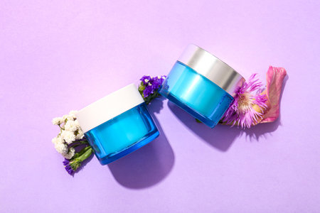 Composition with jars of cosmetic products and flowers on lilac backgroundの写真素材