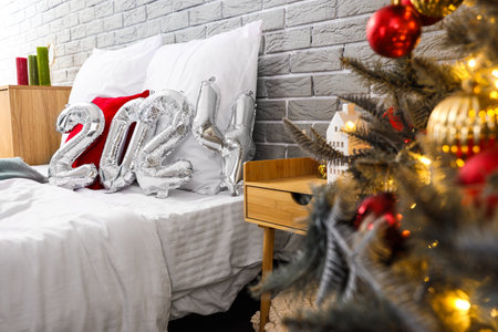 Balloons in shape of figure 2024 on comfortable bed in festive bedroom with Christmas decorの写真素材