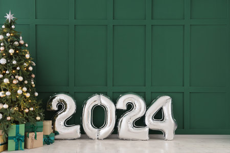 Balloons in shape of figure 2024 and Christmas tree with gifts near green wallの写真素材