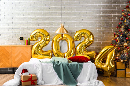 Balloons in shape of figure 2024 on comfortable bed in festive bedroom with Christmas decorの写真素材