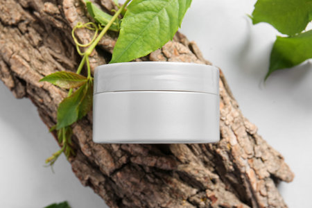 Composition with jar of cosmetic product, tree bark and plant branch on light background, closeup