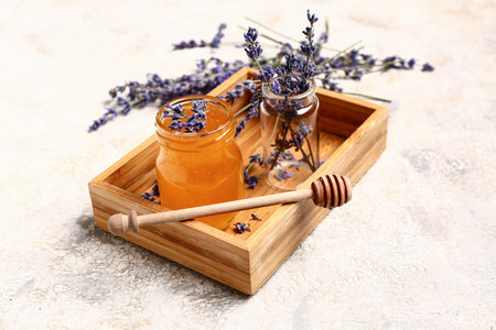 Wooden box with jar of sweet lavender honey, dipper and flowers on white backgroundの写真素材
