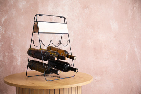 Holder with bottles of wine on wooden table in room near grunge pink wallの写真素材