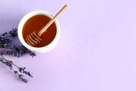 Bowl of sweet lavender honey, dipper and flowers on lilac backgroundの写真素材