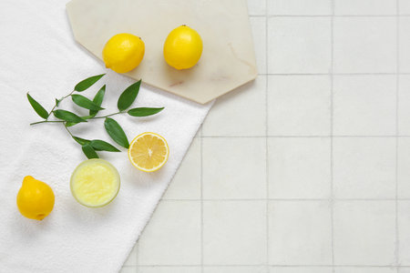 Bowl of lemon body scrub with board and towel on white tile backgroundの写真素材