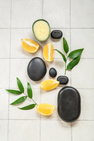Bowl of lemon body scrub with spa stones and plant branches on white tile backgroundの写真素材