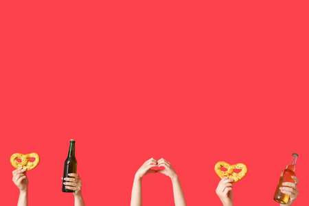Many hands with bottles of cold beer and pretzels on red backgroundの写真素材
