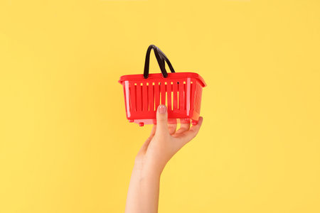Woman holding mini shopping basket on yellow backgroundの写真素材