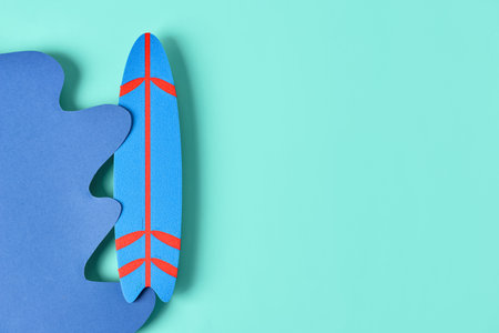 Creative composition with paper wave and mini surfboard on turquoise backgroundの写真素材