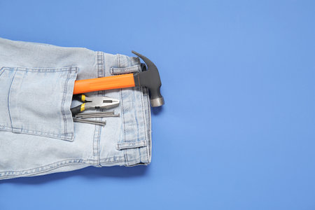 Hammer, pliers and nails in jeans pocket on blue background. labor day celebrationの写真素材