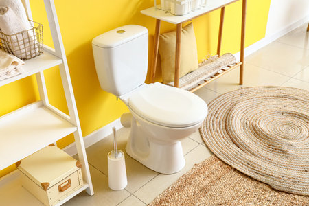 Interior of modern restroom with ceramic toilet bowl and paper holder near yellow wall